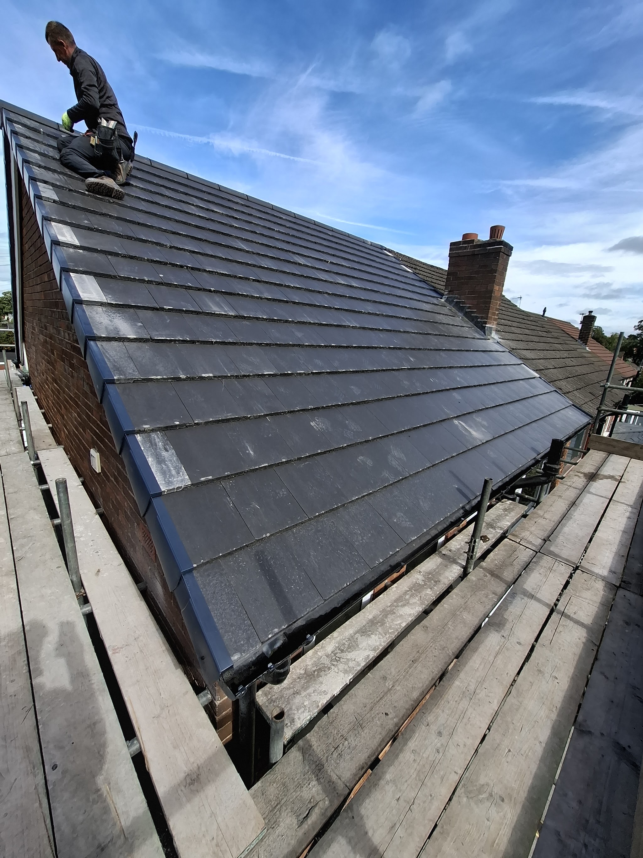 A finished grey slate roof by M.D Roofing, with a roofer at the ridge