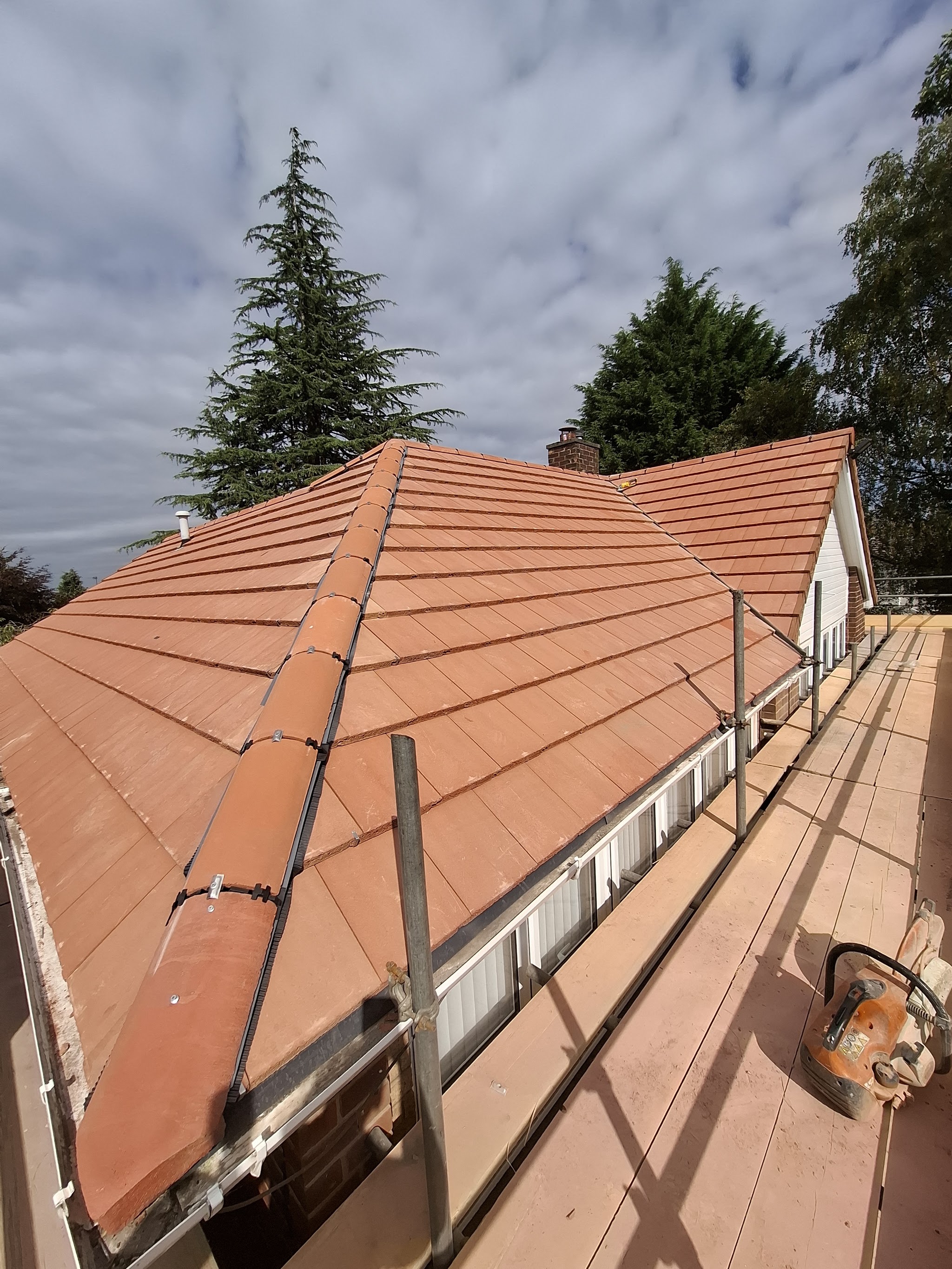 A finished red tiled hip roof with a new ridge, seen from the scaffold