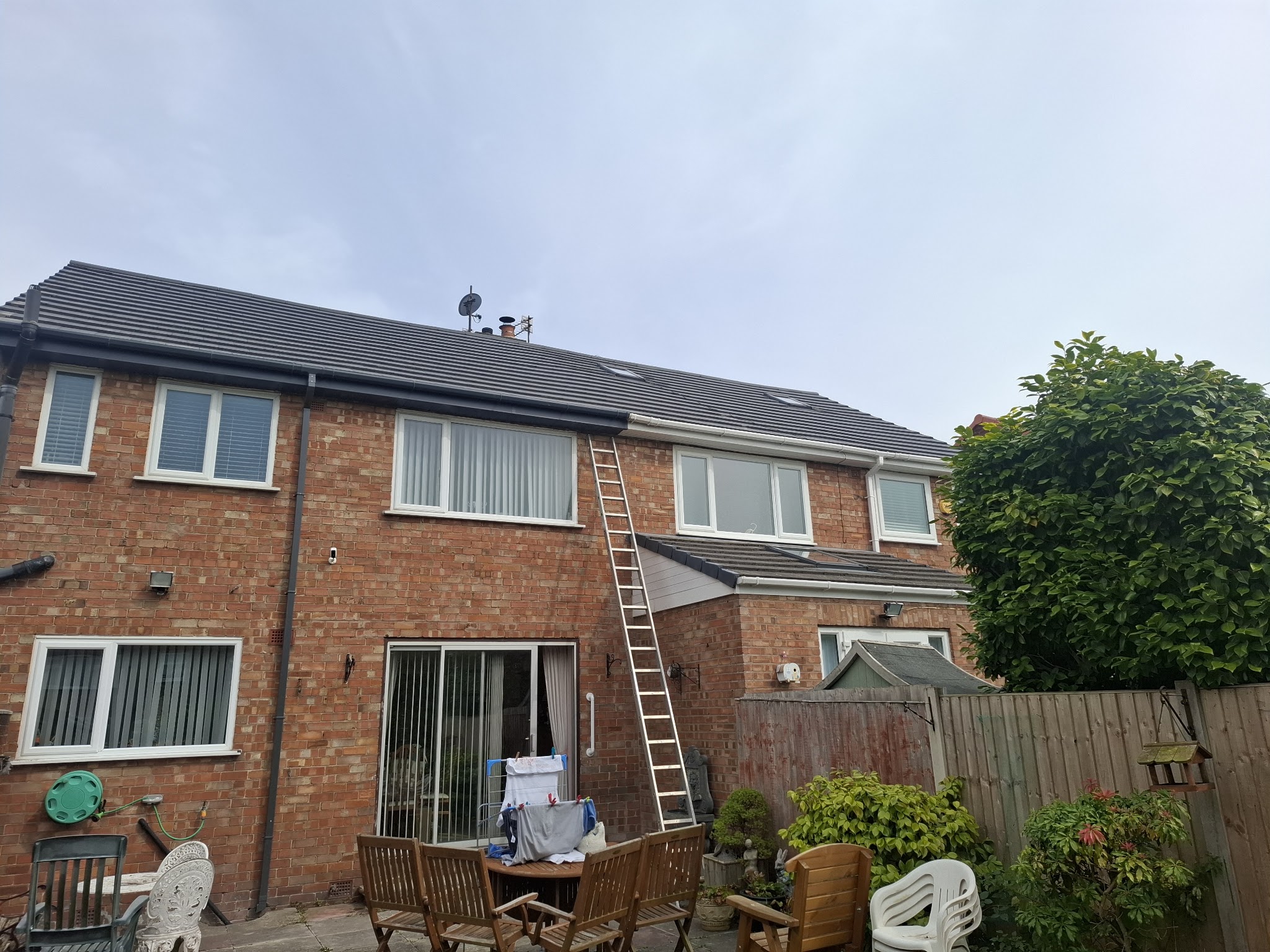 A finished grey tiled roof on a brick house, seen from the back garden